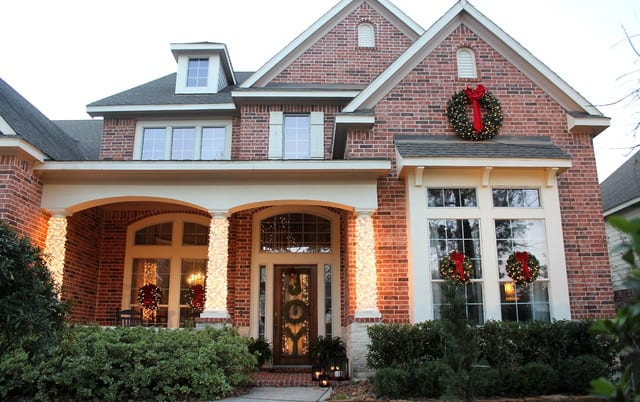 this shows a simple traditional set of holiday lights and holly on a brick house