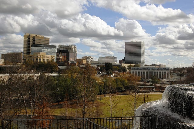 A view of the Columbia South Carolina skyline overlooking a park with fountain and trees.
