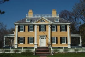 Large yellow colonial house with black shutters and white columns.