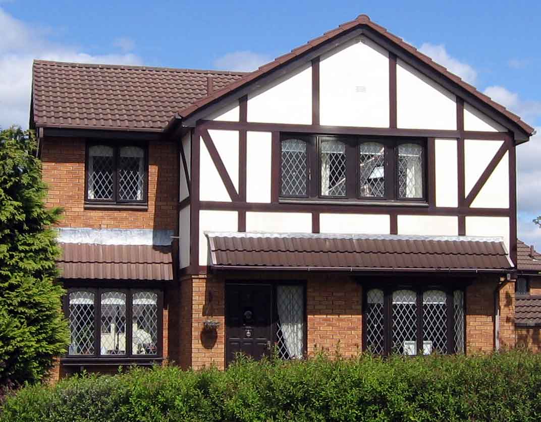 Tudor house with white and brown siding and brick foundation.
